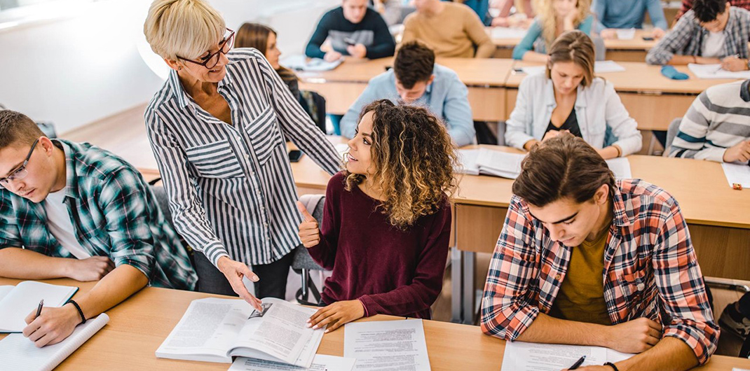 photo of a professor discussing course material with a student in a higher education classroom