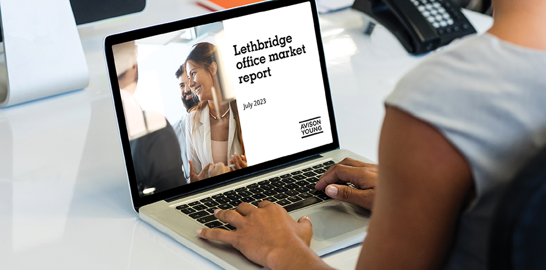 photo of a laptop on a table with a person's hands on the keyboard, the screen displays Avison Young's Lethbridge office market report July 2023
