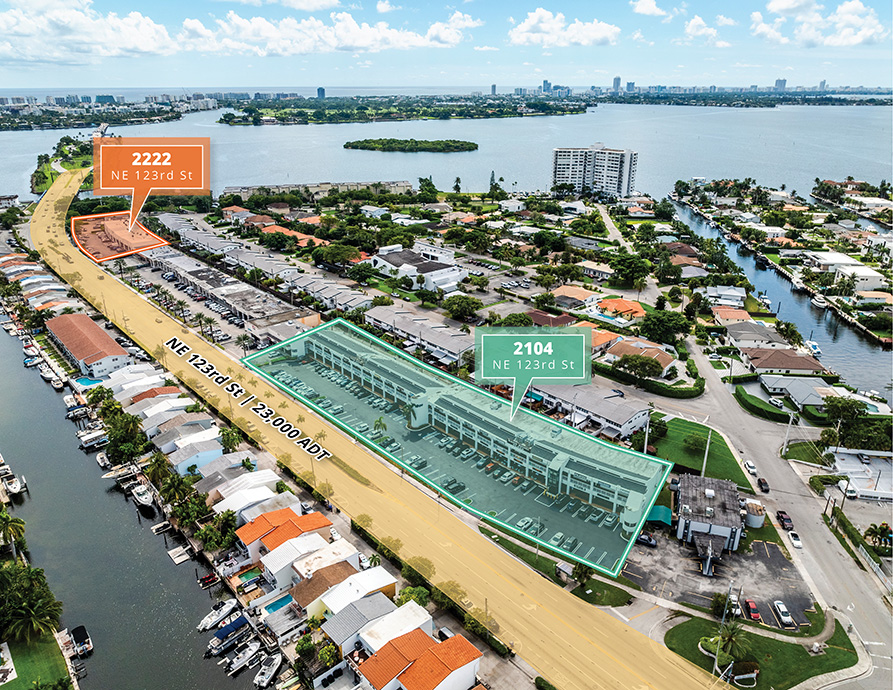 drone view of retail buildings and houses on a canal in Sans Souci Plaza with the ocean in the background located in North Miami, Florida